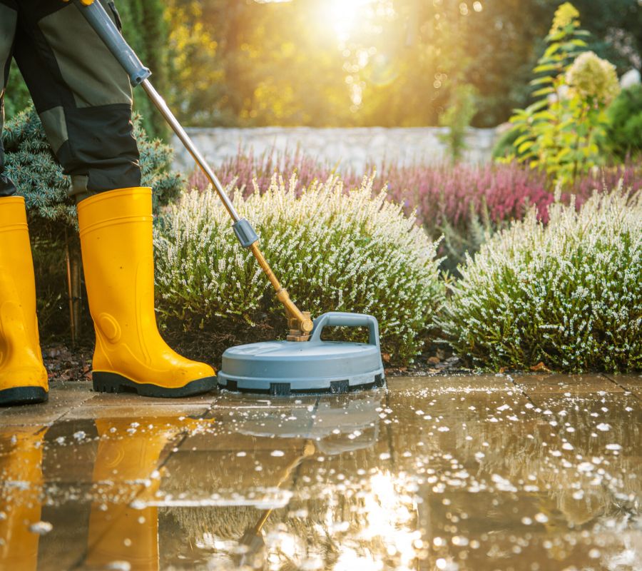 Person Using An Outdoor Pressure Washer On A Patio In A Garden During Sunny Weather