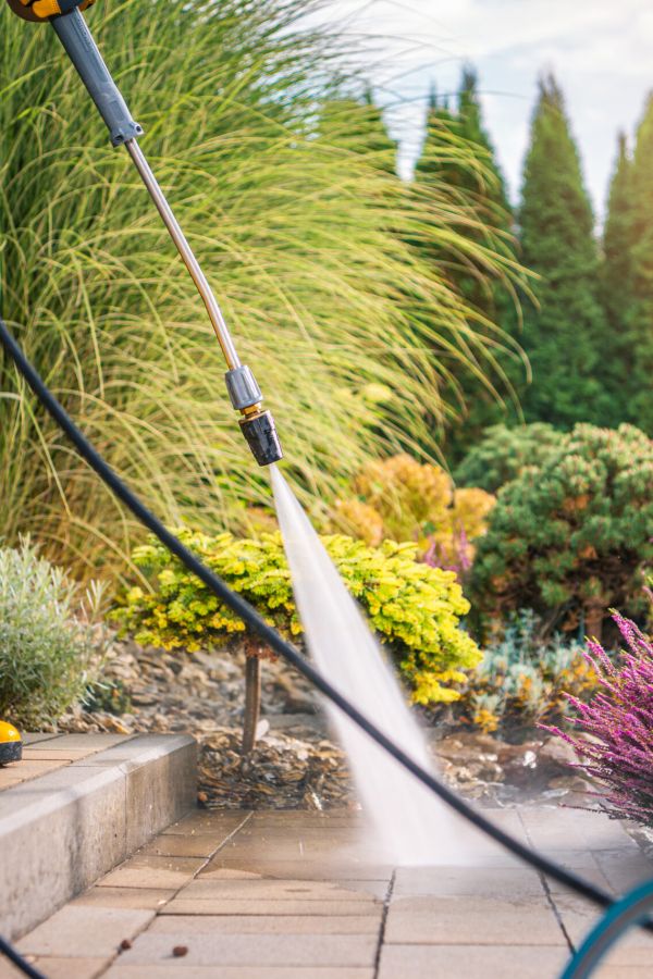 Person Cleaning Patio With Pressure Washer During Sunny Day In Garden Landscape