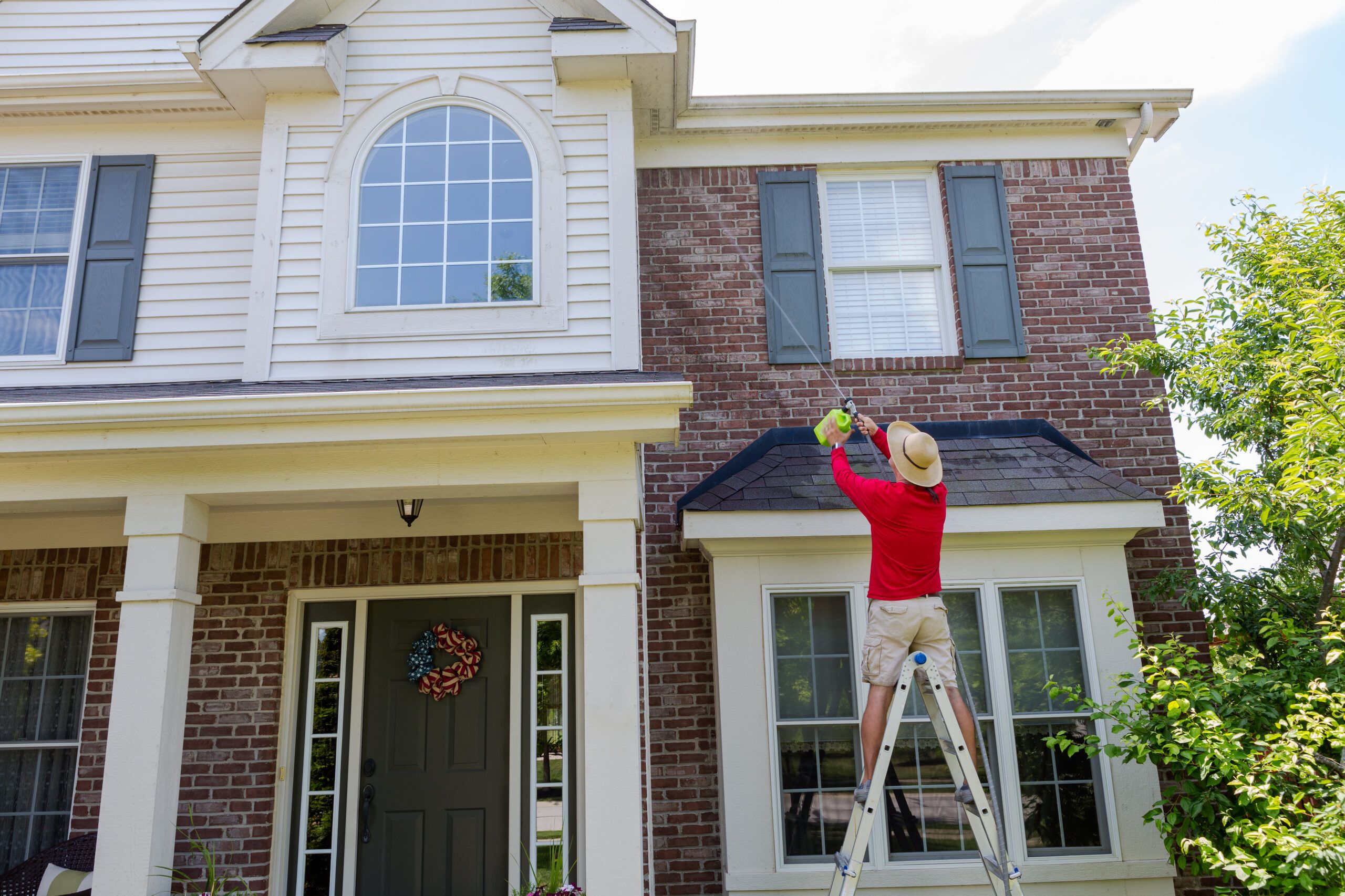 Man Washing The Soffits Or Eaves Of A Modern House